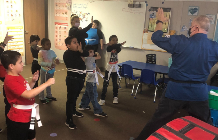 Children in fighting stance with Karate instructor demonstrating hand position.